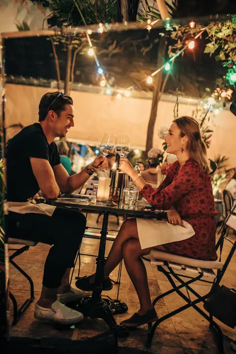 Ein Paar stößt bei Kerzenlicht im Gastgarten mit Wein an