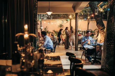Gäste beim Dinner im Gastgarten bei Nacht, Lichterketten zwischen den Bäumen