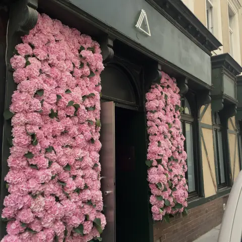 Die Fassade in Margareten — rosa Hortensien rahmen den Eingang mit dem THELL-Neon